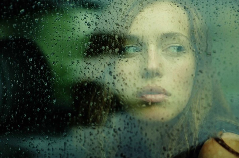 Ảnh chụp người phụ nữ nhìn ra trời mưa qua ô cửa sổ